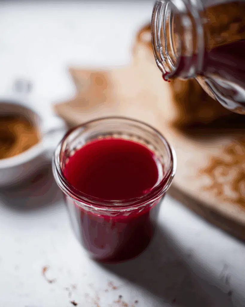 Jar of vibrant red shrub concentrate being poured